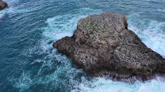 空中倾斜向下拍摄海面上的岩层，无人机在溅起的海浪上向前飞行——西班牙马略卡岛视频素材