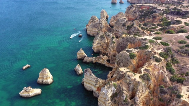 在晴朗的日子里，空中倾斜向下拍摄岩石嶙峋的海岸线，无人机在葡萄牙拉各斯海的悬崖上向前飞行视频素材