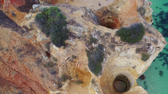 葡萄牙拉各斯，空中倾斜拍摄海滩上岩石峭壁上的游客，无人机沿着海岸楼梯向前飞过人们视频素材