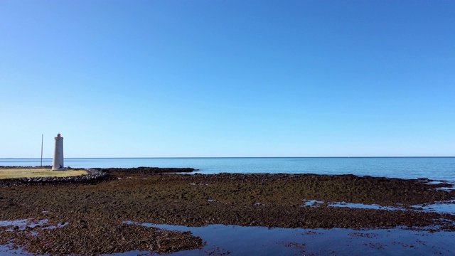 航拍:在晴朗的日子里，无人机在冰岛雷克雅未克附近的岩石群上空拍摄著名的海上灯塔视频素材