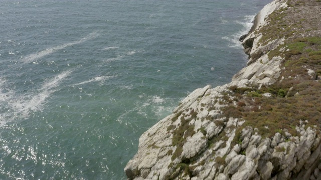 航拍鸟类飞过岩石形成在海上，无人机向前飞行在海浪溅在岩石悬崖在阳光明媚的一天-阿尔加维，葡萄牙视频素材