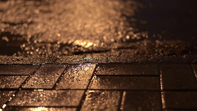 雨夜的城市街道，雨水在路灯下的人行道上流淌。视频素材