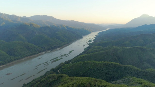 空中拍摄的河流在郁郁葱葱的绿色山脉对天空，无人机飞在森林的树木在日出-琅勃拉邦，老挝视频素材