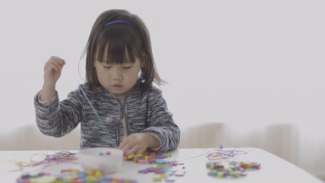 蹒跚学步的女孩串木珠工艺品在家上学视频素材