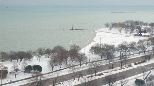 车辆在芝加哥湖滨车道上行驶，人们在密歇根湖沿岸的空地上移动，白雪覆盖了地面，海浪滚滚而来。视频素材