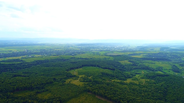 无人机从森林覆盖的山坡后面飞行，在阳光明媚的夏日打开山村壮丽的景色。视频素材