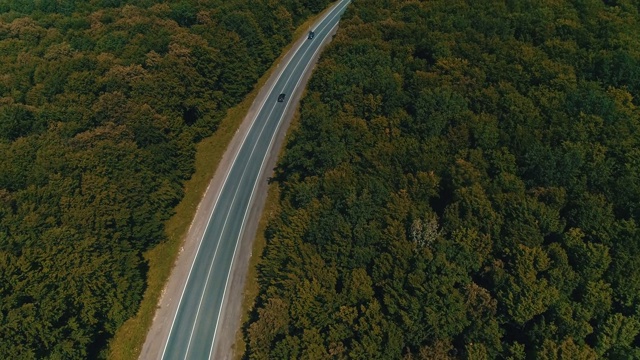 无人机飞过老森林道路与汽车移动，绿树茂密的树林两侧生长。视频素材