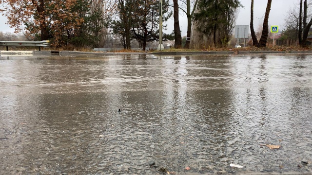 秋天的雨天，城市交通在潮湿的道路上行驶，汽车驶过一个车轮溅起水花的水坑。视频素材