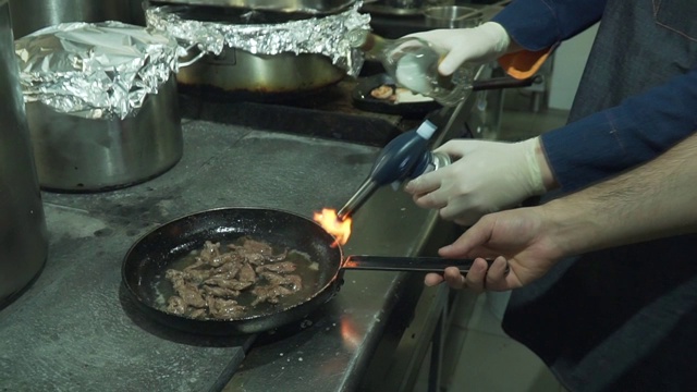 一个专业的厨师准备饭菜。锅里的肉烧焦了。在锅中烧油。的食物视频素材