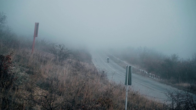 浓雾笼罩着山里的道路，一个骑摩托车的人在这条路上行驶视频素材