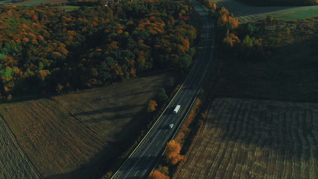 鸟瞰图相机在秋天的田野之间跟随白色货车行驶的道路。视频素材