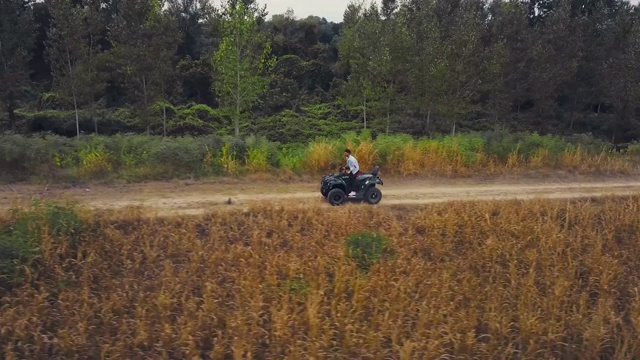 在乡村公路上驾驶Quad汽车的人。穿着休闲的男人骑着一辆黑色四轮车。视频下载