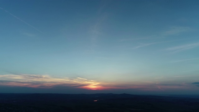 红橙色的日落云景在蓝色的夜空与山的剪影在地平线和飞机的痕迹。视频素材