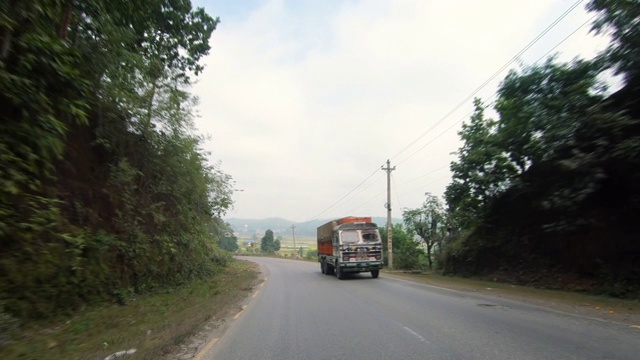 摩托车上的POV沿着乡村道路，都覆盖着树木和稻田。视频下载