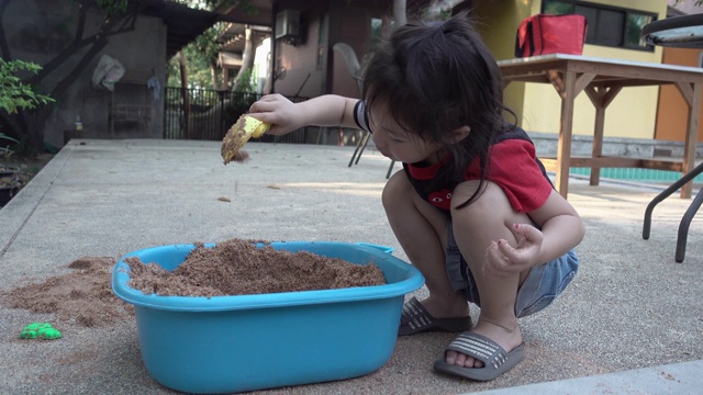 亚洲小女孩一起在院子里玩沙子玩得很开心。真实生活，手持拍摄视频下载