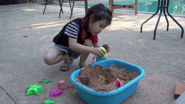 亚洲小女孩一起在院子里玩沙子玩得很开心。真实生活，手持拍摄视频下载