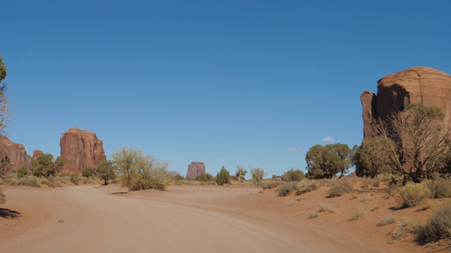 在纪念碑谷的红岩间的沙漠中尘土飞扬的道路上行驶视频素材