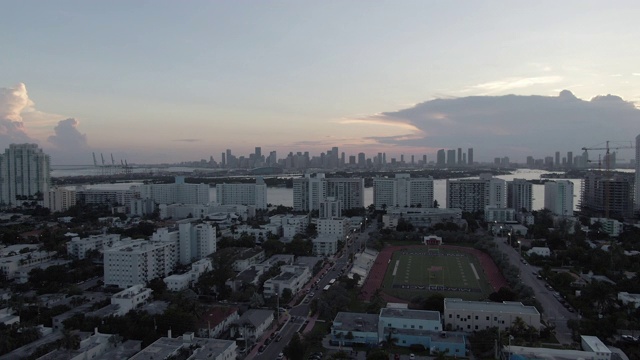 航拍的体育场在城市的街道上，在海上对着天空，无人机向后飞行的建筑物在日落-迈阿密，佛罗里达视频素材