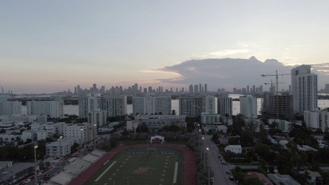 空中平移拍摄的体育场在城市的街道在海上对天空，无人机飞过建筑物在日落-迈阿密，佛罗里达视频素材