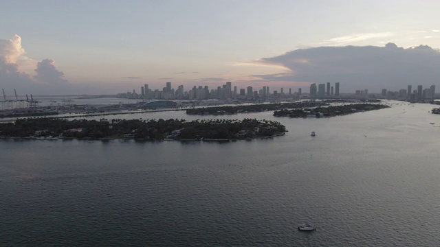 空中倾斜拍摄岛屿附近海面上的船只，日落时无人机从城市向后飞行——迈阿密，佛罗里达视频素材