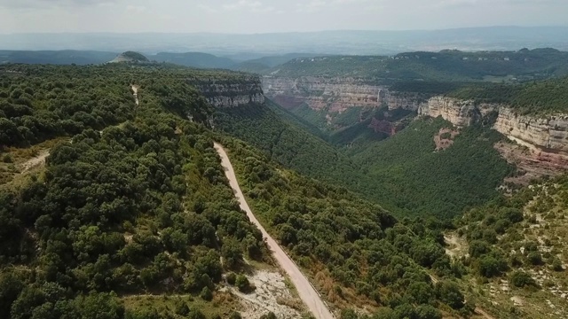 航拍的岩石山与绿色植物的天空，无人机上升的自然景观与汽车在晴朗的一天-塔弗泰，西班牙视频素材