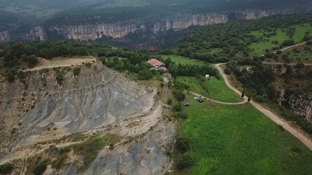 航拍山上树木中的建筑物和车辆，无人机在绿色景观上向前飞行——西班牙塔弗泰视频素材