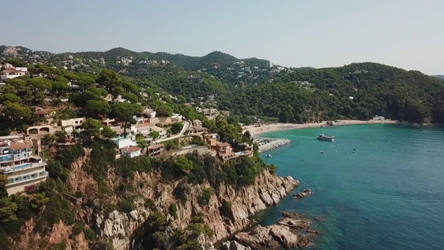 在阳光明媚的日子里，无人机在多岩石的海岸线上空拍摄悬崖上的房屋视频素材