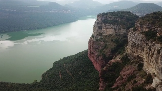 航拍岩石悬崖与河流附近的植物，无人机向前飞行的自然景观-塔弗泰特，西班牙视频素材