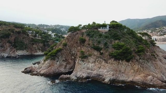 航拍在岩石上的植物中拍摄的历史地标，无人机在城市附近的海上对着天空飞行- Tossa de Mar，西班牙视频素材