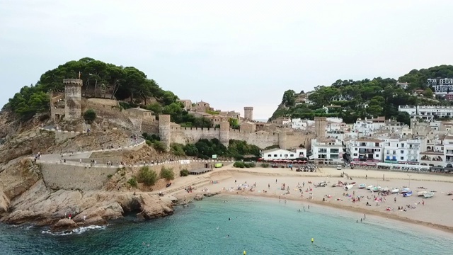 空中拍摄海滩上历史古堡的人对着天空，无人机飞过海洋的城市- Tossa de Mar，西班牙视频素材