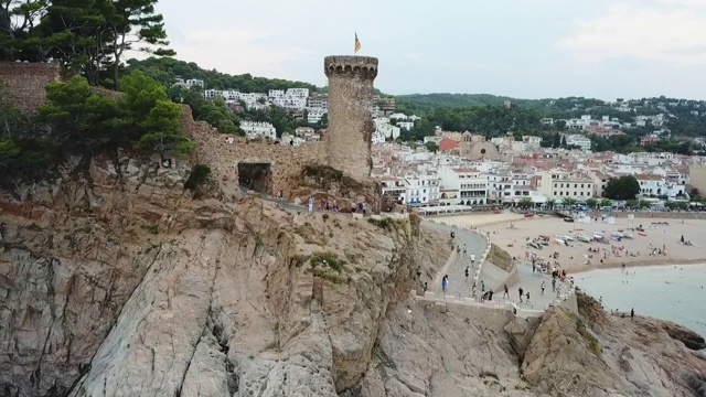 航拍游客在岩石上的历史堡垒，无人机在天空下降落在城市附近- Tossa de Mar，西班牙视频素材