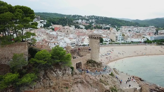 航拍游客在岩石形成的历史堡垒，无人机从城市向后飞行的天空- Tossa de Mar，西班牙视频素材