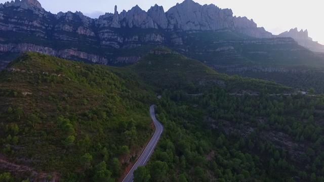 航拍的道路上的车辆在植物对山，无人机飞向前绿色景观-蒙特塞拉特，西班牙视频素材