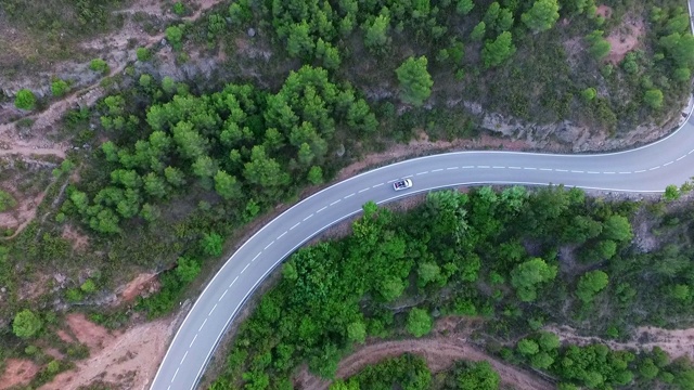 空中倾斜拍摄的汽车在道路上的树木对岩石山脉，无人机飞过自然绿色景观-蒙特塞拉特，西班牙视频素材