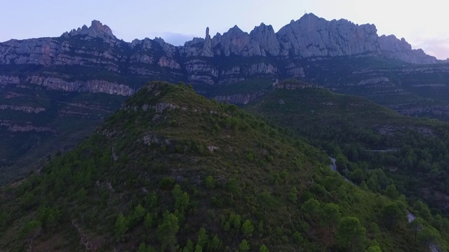 航拍的岩石山脉对天空在日落，无人机上升在绿色景观-蒙特塞拉特，西班牙视频素材