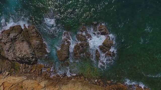 在阳光明媚的日子里，海浪拍打在海上的岩石上的鸟瞰图，无人机在岩石上上升-略雷特德马尔，西班牙视频素材