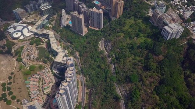 航拍街道上的车辆在树木和建筑物之间，无人机向前飞行城市通过海上在阳光明媚的一天-中国香港视频素材