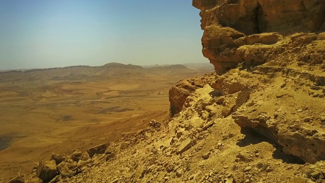 在一个晴朗的日子里，无人机在干旱的土地上向前飞行，在沙漠中拍摄岩石山，以色列米茨佩拉蒙视频素材