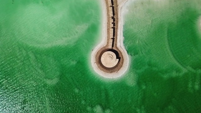 鸟瞰游客在盐湖游泳，无人机飞过碧绿死海码头上的凉亭视频素材