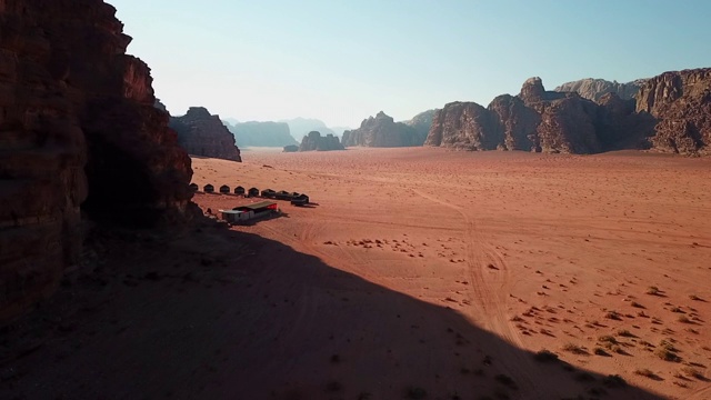 空中平移拍摄帐篷的岩石悬崖在沙漠对天空，无人机飞过干旱的景观在晴朗的一天-瓦迪拉姆，约旦视频素材