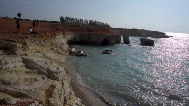 在塞浦路斯岛帕福斯，阳光明媚的日子里，从海上对着天空摇摄岩石悬崖上的游客视频素材