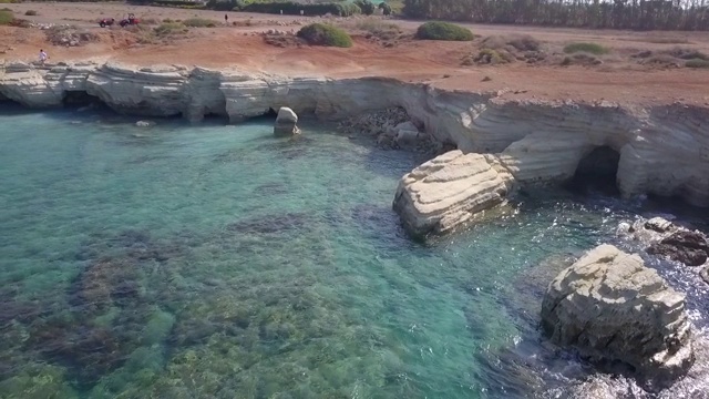 在阳光明媚的日子里，无人机在沉船附近的蓝色水域上空拍摄岩石海岸线，帕福斯，塞浦路斯视频素材