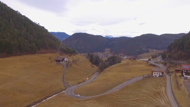 航拍在山谷村庄附近的道路上的车辆，无人机飞向天空中的山脉- Dolomites，意大利视频素材