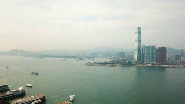 空中平移拍摄的船只在海上由现代建筑对天空，无人机飞越沿海城市附近的山区-香港，中国视频素材