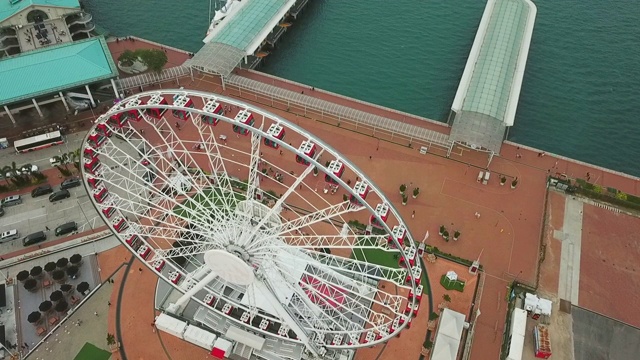 空中倾斜拍摄海上摩天轮对着天空，无人机在沿海城市-中国香港上空降落视频素材