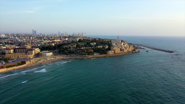 日落时，空中拍摄的城市，无人机在建筑物附近的波浪上飞行-雅法，以色列视频素材