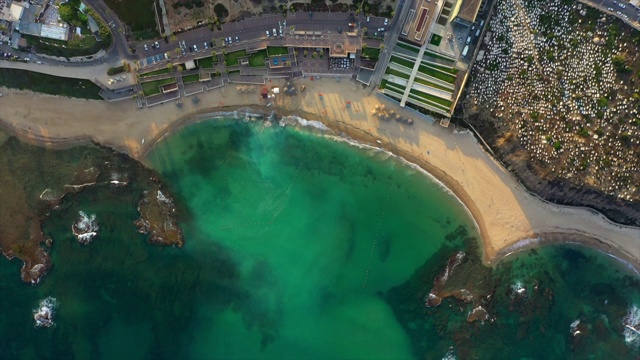 鸟瞰图拍摄的海滩在城市与绿松石海日落，无人机飞过海岸线-雅法，以色列视频素材