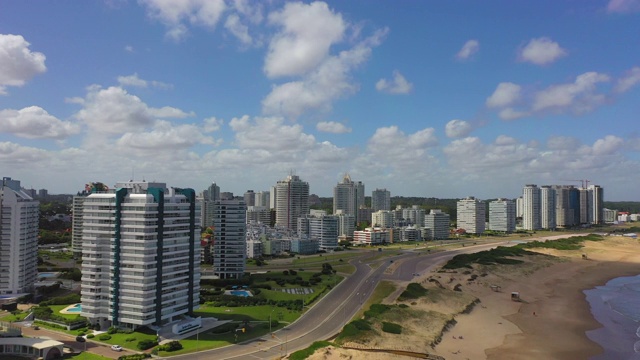 航拍街道和海滩上的建筑，以天空为背景，无人机从城市的住宅建筑中向后飞行——乌拉圭埃斯特角视频素材