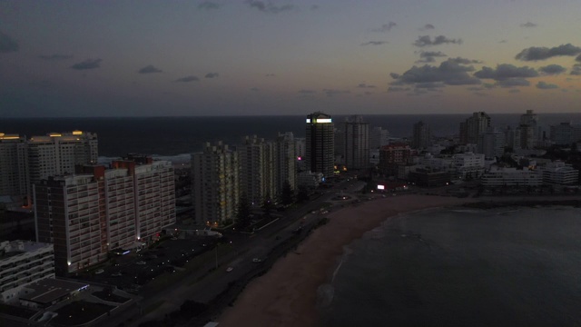 航拍向前拍摄的城市在黄昏的海滩上的天空，无人机向前飞行的海洋-埃斯特角，乌拉圭视频素材