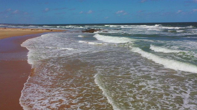 航拍:在阳光明媚的日子里，海浪拍打在海滩上的慢镜头——乌拉圭埃斯特角视频素材